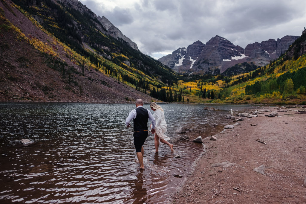 A couple holds hands playing in the water during their maroon bells elopement.