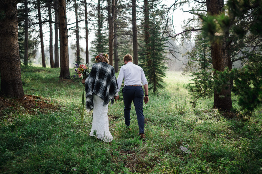 A couple walks hand in hand through the colorado everreen trees for their elopement.