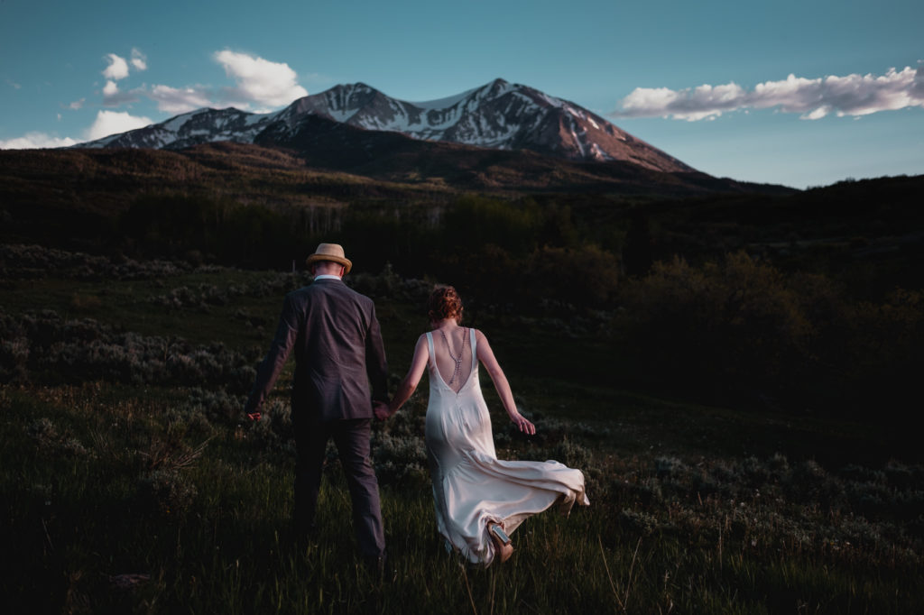 Bride and groom run towards a mountain after they elope in Colorado.